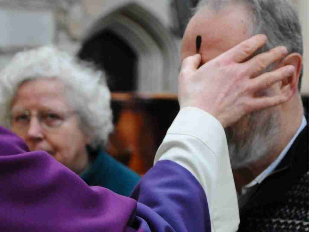 A Bath Abbey member of clergy placing an ash cross on a worshipper's forehead