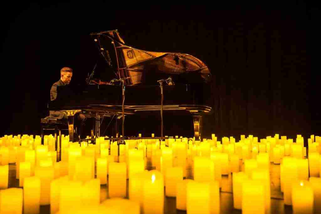 Man playing the piano surrounded by lit candles