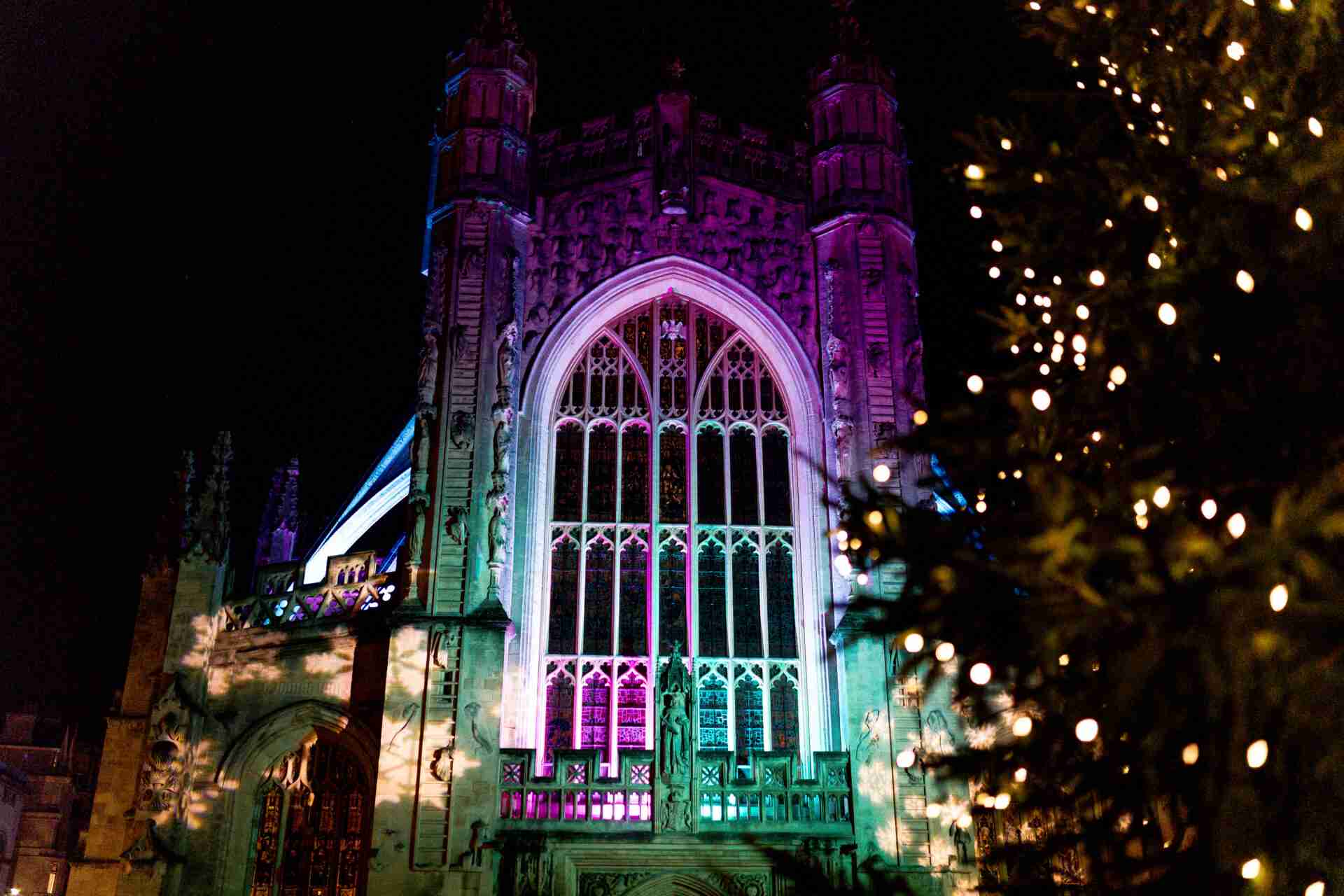 Bath Abbey lit up with colourful lights and a Christmas Tree with gold lights