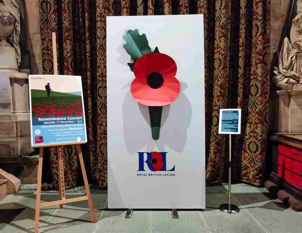 Giant paper poppy for Remembrance next to a poster for a concert and a Remembrance prayer