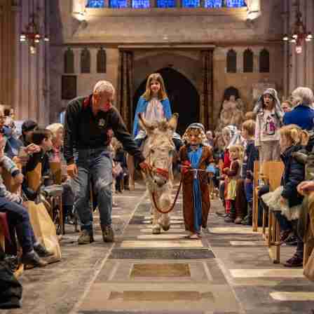 Children dressed up for the Nativity in Bath Abbey as Mary and Joseph with Mary riding Dermot the Donkey down the Nave