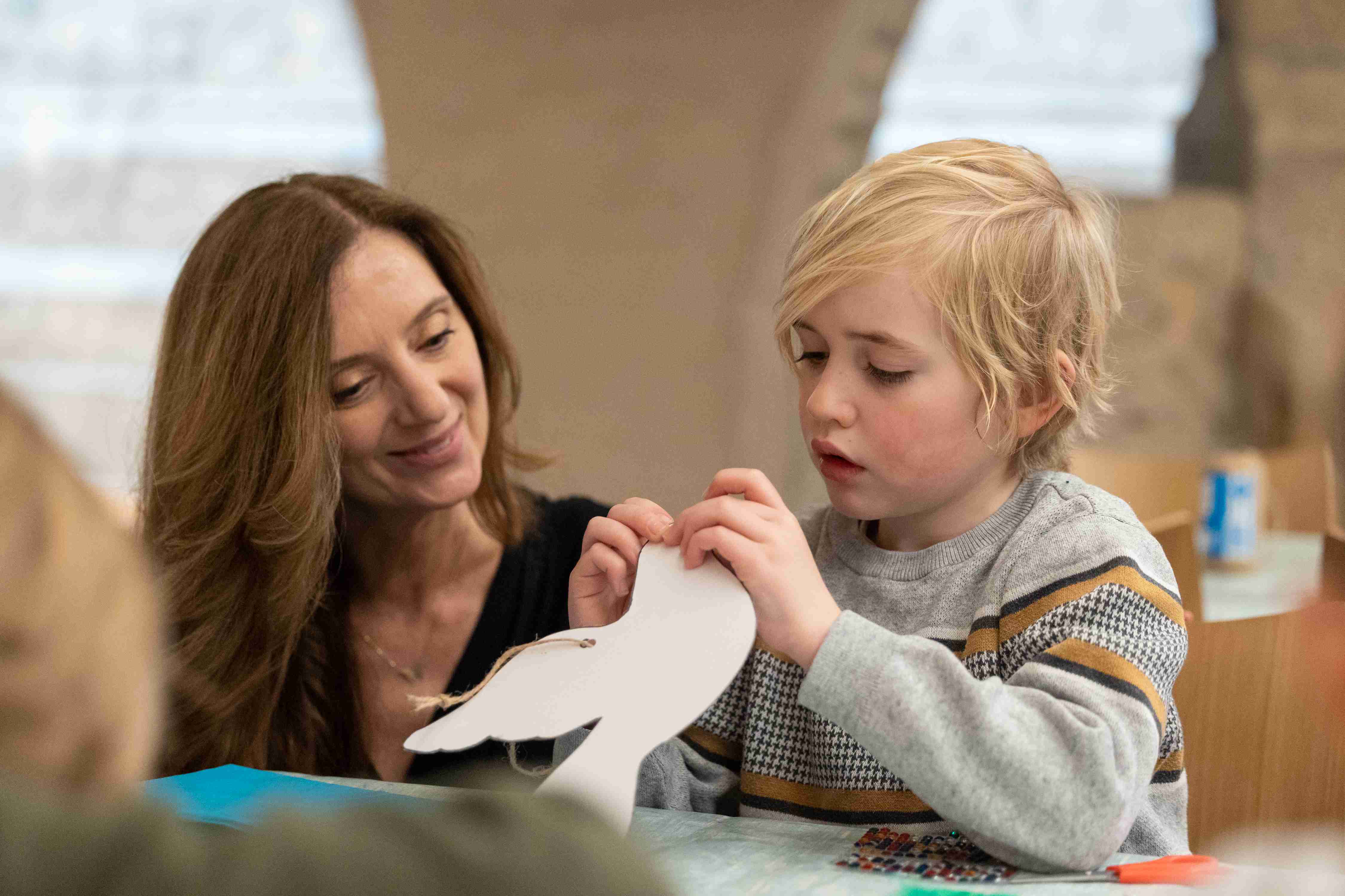 A woman talks to a child doing a craft activity